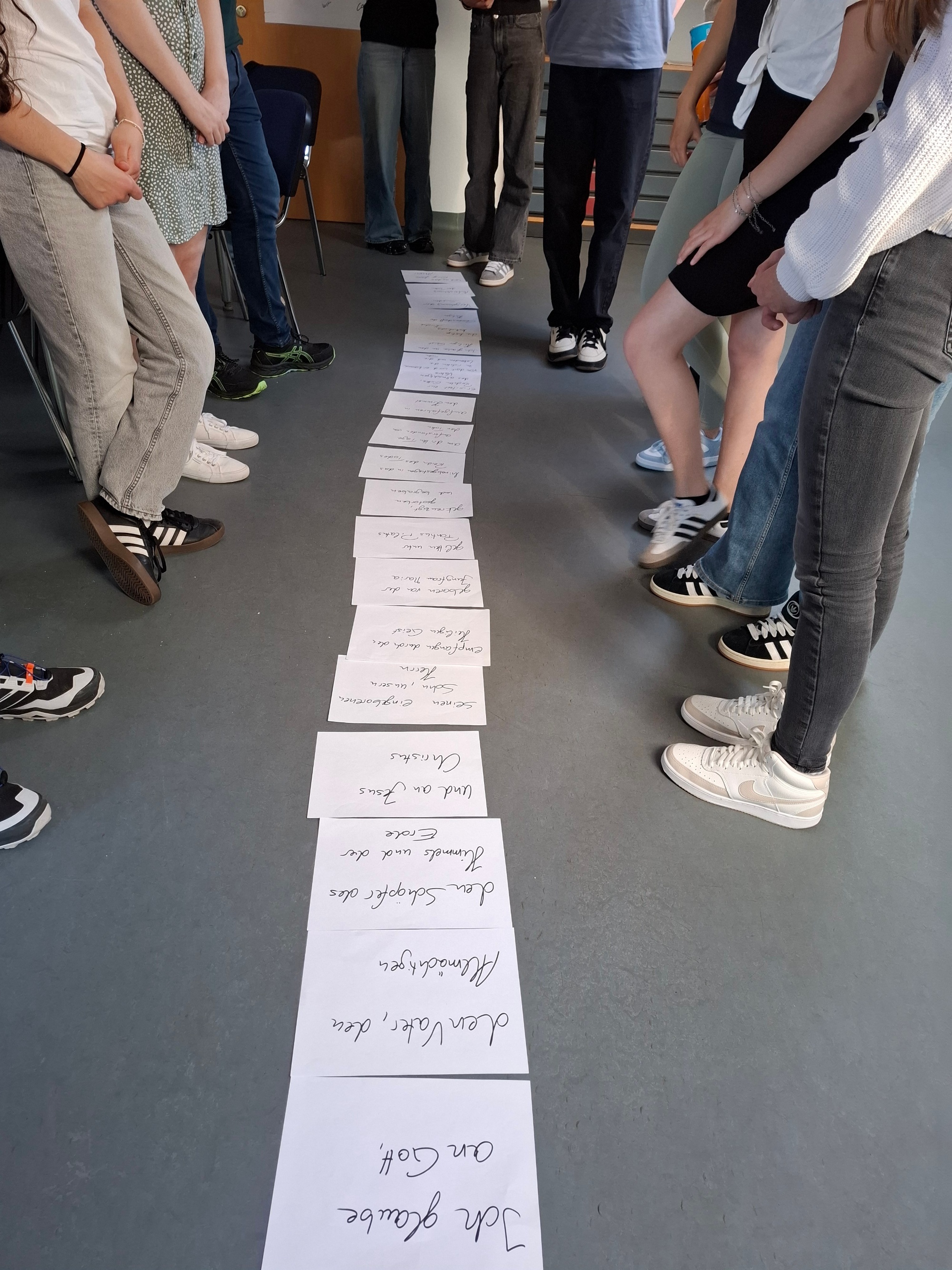 Mehrere Personen stehen um eine Reihe von beschrifteten Papierbögen auf dem Boden.