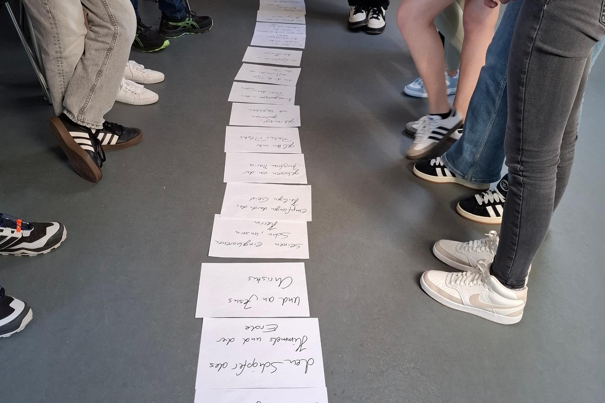 Mehrere Personen stehen um eine Reihe von beschrifteten Papierbögen auf dem Boden.