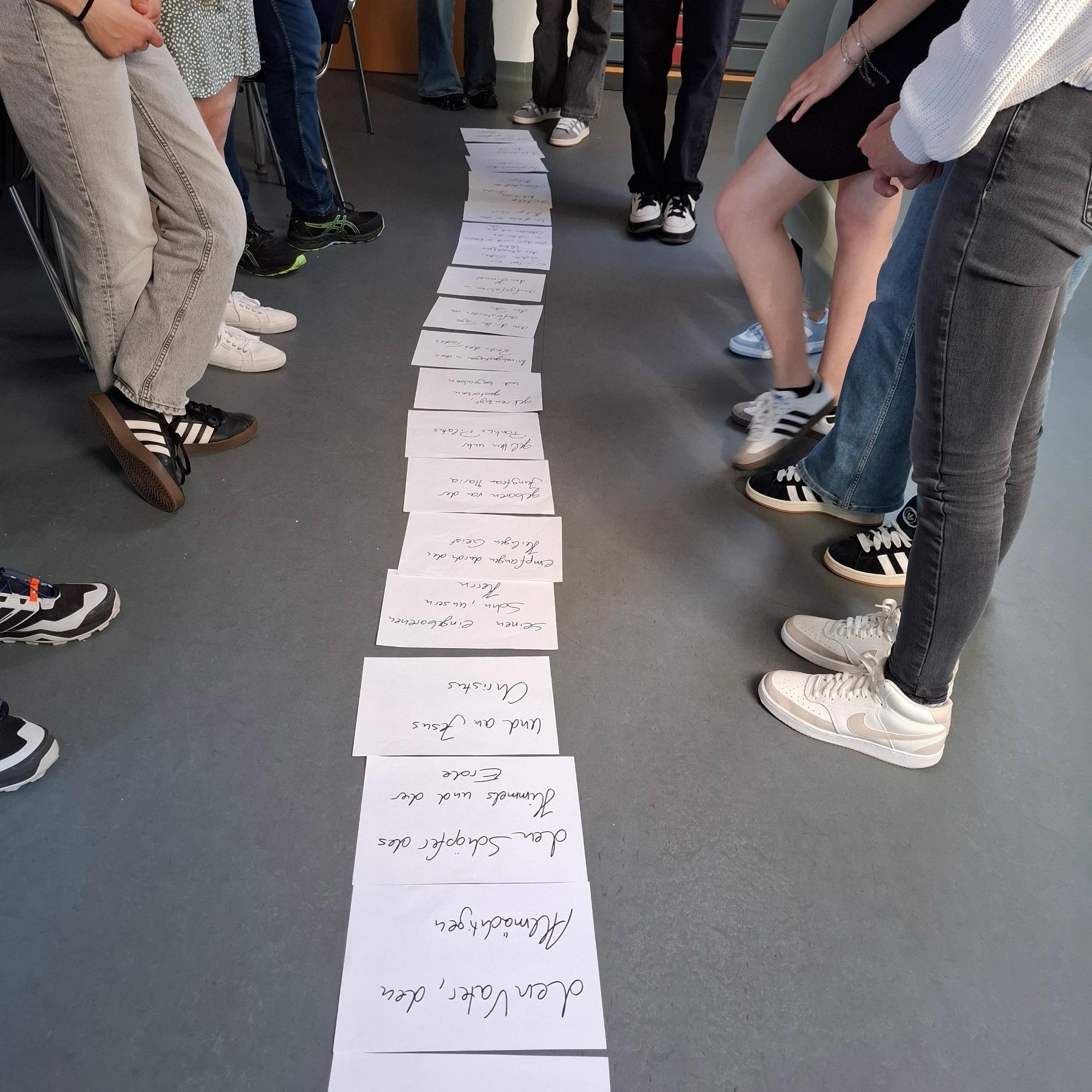 Mehrere Personen stehen um eine Reihe von beschrifteten Papierbögen auf dem Boden.